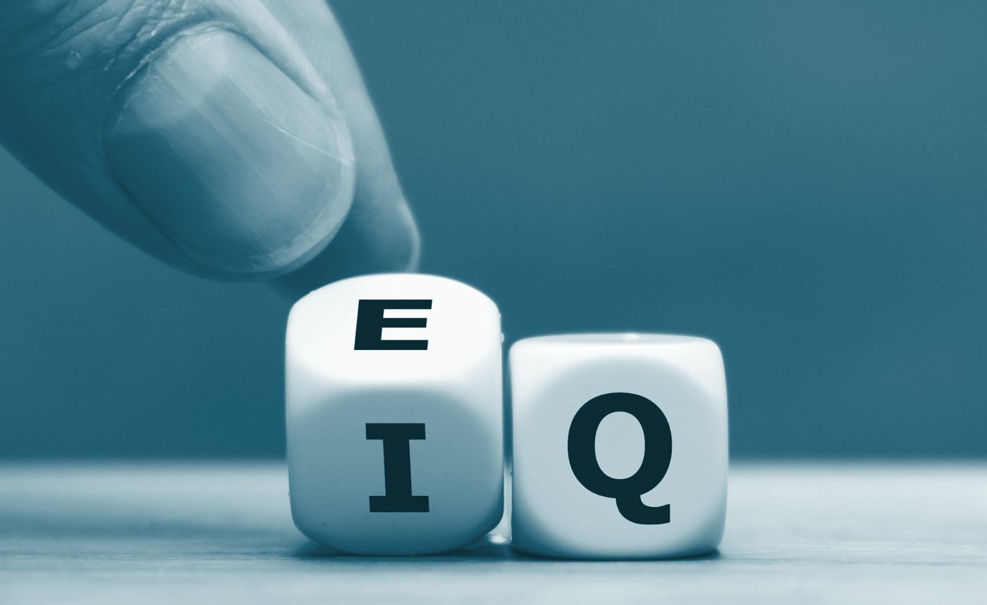 A hand turning a die so the letters read EQ instead of IQ